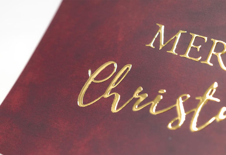 Close-up van een bordeauxrode kerstkaart met "Merry Christmas" in elegante goudfolie letters, waarin de feestelijke personalisatie wordt benadrukt.