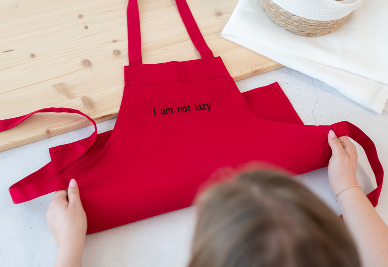 Rød barneforkle med "I am not lazy" tekst i svart på forsiden.