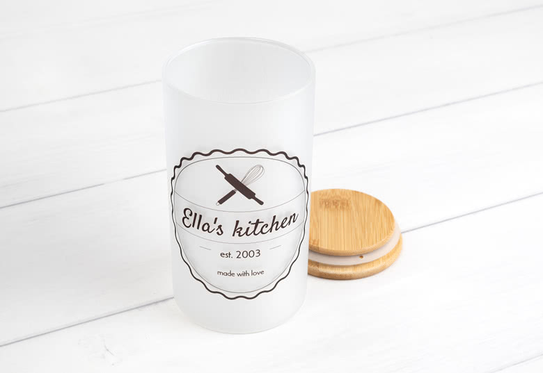 Gepersonaliseerde witte voorraadpot met houten deksel, met de tekst "Ella's kitchen" en grafische afbeeldingen van keukengerei in het zwart.