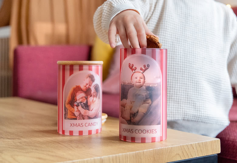 Gepersonaliseerde rood-wit gestreepte voorraadpotten met de labels "Xmas Candy" en "Xmas Cookies" en gepersonaliseerde foto's op een houten tafel.