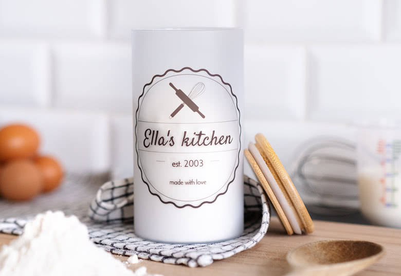 Personlig vit glasburk med texten "Ella's kitchen" och grafik av köksredskap. Anpassningsbara detaljer inkluderar namn och årtal.