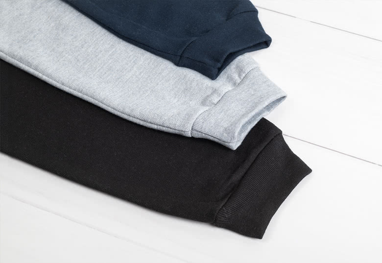 Stak af tre personlige sweatshirts i marineblå, grå og sort, foldet på en hvid overflade.