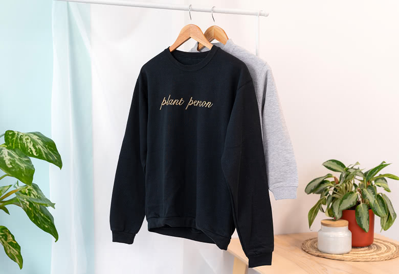 Black and grey sweatshirts with 'plant person' text, hanging on wooden hangers.